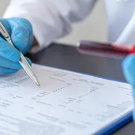 Image of hands with gloves holding blood test and checking a list